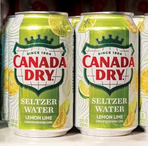Cans of Canada Dry lemon lime seltzer water are displayed on a shelf next to a plastic bottle of purified water. The green cans, adorned with lemons and limes, make a refreshing Family First choice in BC households.