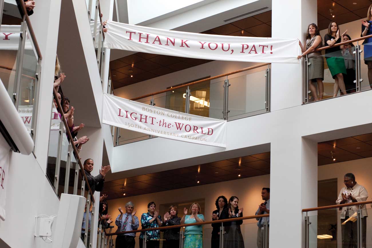 People stand on balconies inside a building, holding banners that say "THANK YOU, PAT!" and "LIGHT the WORLD 150th ANNIVERSARY CAMPAIGN." Some are clapping and smiling in celebration, their faces shining with gratitude during this meaningful Act of Gratitude.